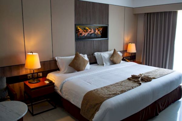 This image shows a modern hotel room with a large bed, two bedside tables with lamps, and a decorative wall piece above the headboard.