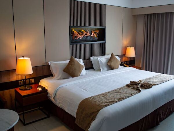 This image shows a modern hotel room with a large bed, two bedside tables with lamps, and a decorative wall piece above the headboard.
