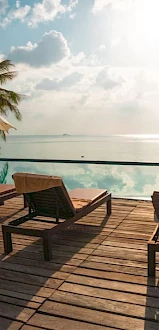 A serene poolside setting with lounge chairs, palm trees, umbrellas, and a tranquil ocean view on a sunny day, ending the sentence.
