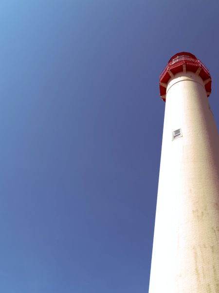 The image shows a tall lighthouse with a red top, set against a clear blue sky.