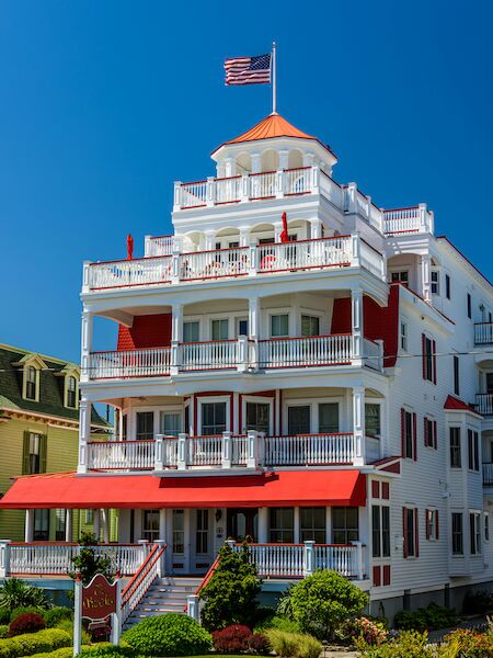 A large, multi-story building with a red and white color scheme, featuring balconies and a U.S. flag on top, surrounded by greenery.