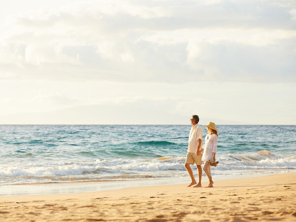 A couple is walking along a sandy beach by the ocean, under a partly cloudy sky, enjoying a peaceful moment together.
