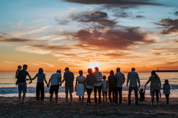 A group of people are standing on a beach during sunset, holding hands and facing the ocean, enjoying the beautiful scenery and moment together.