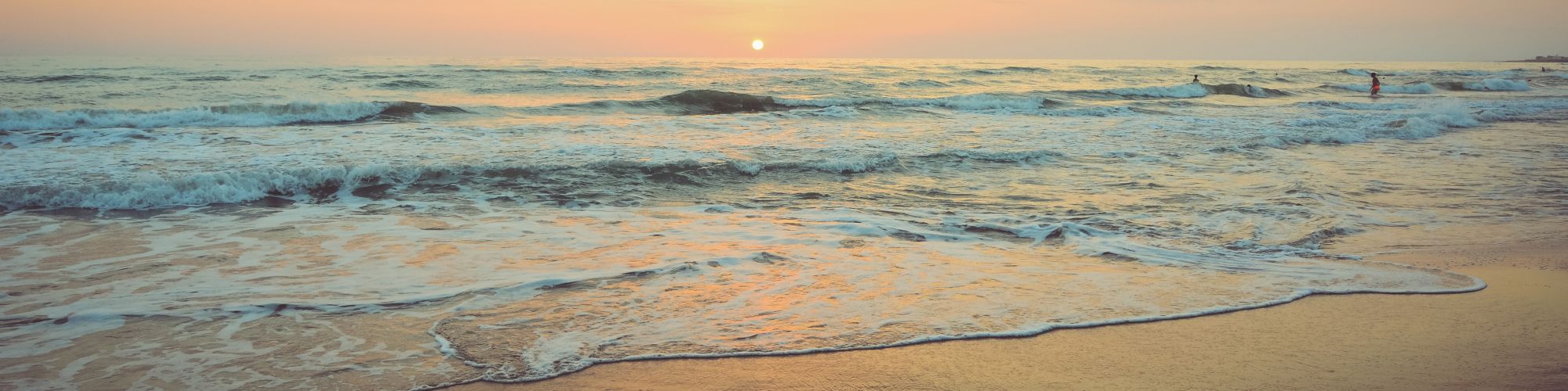 A serene beach scene during sunset with gentle waves, a soft reflection of the sky on wet sand, and a tranquil horizon.