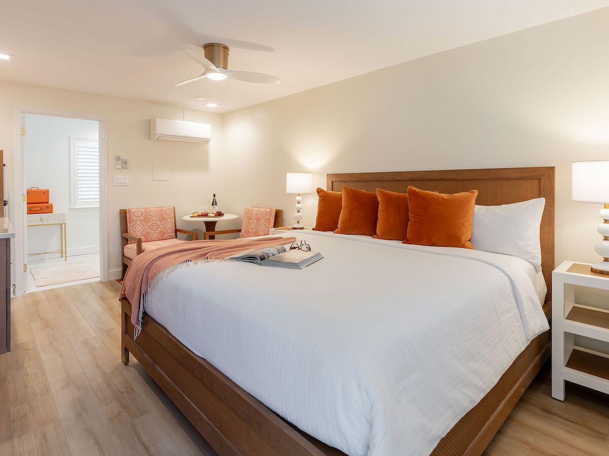 A cozy bedroom featuring a large bed with white and orange decor, two side tables with lamps, a ceiling fan, and a small seating area.