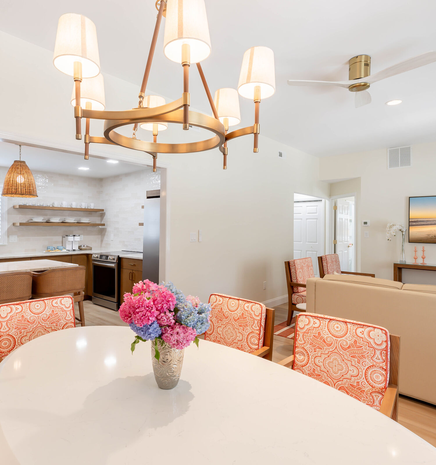 A modern open-concept living area with a dining table, a vase of flowers, a cozy seating area, and a kitchen with pendant lighting.