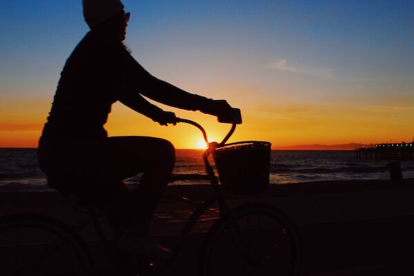 A silhouette of a person riding a bicycle along a waterfront at sunset, with a pier visible in the distance.