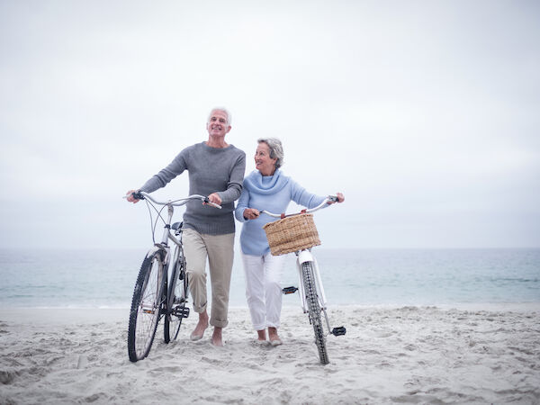 A couple is standing on a beach with bicycles, smiling and enjoying the view, with the ocean in the background.