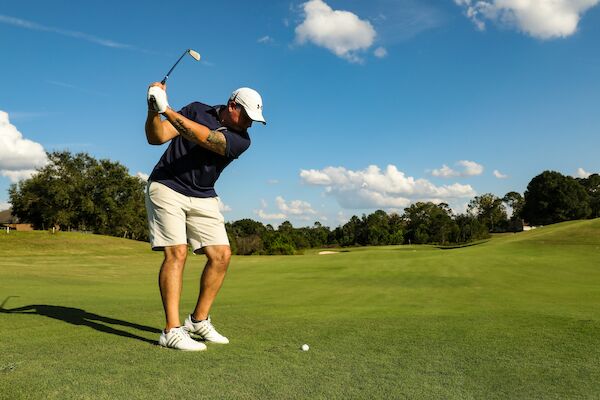 A person is playing golf on a sunny day, preparing to swing with a golf club, on a well-maintained green course.