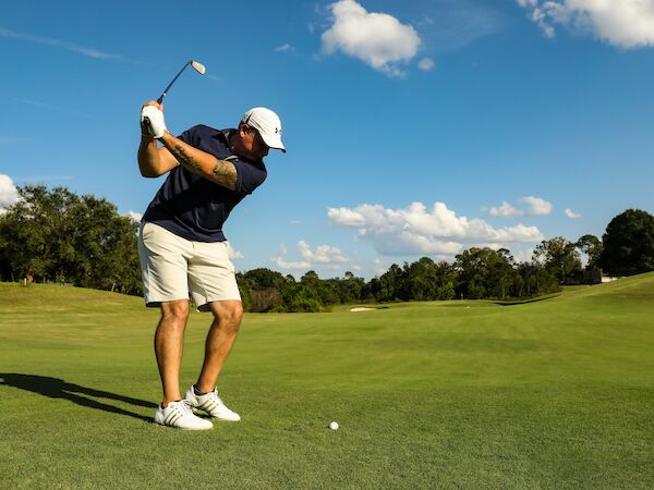 A person is playing golf on a sunny day, preparing to swing with a golf club, on a well-maintained green course.