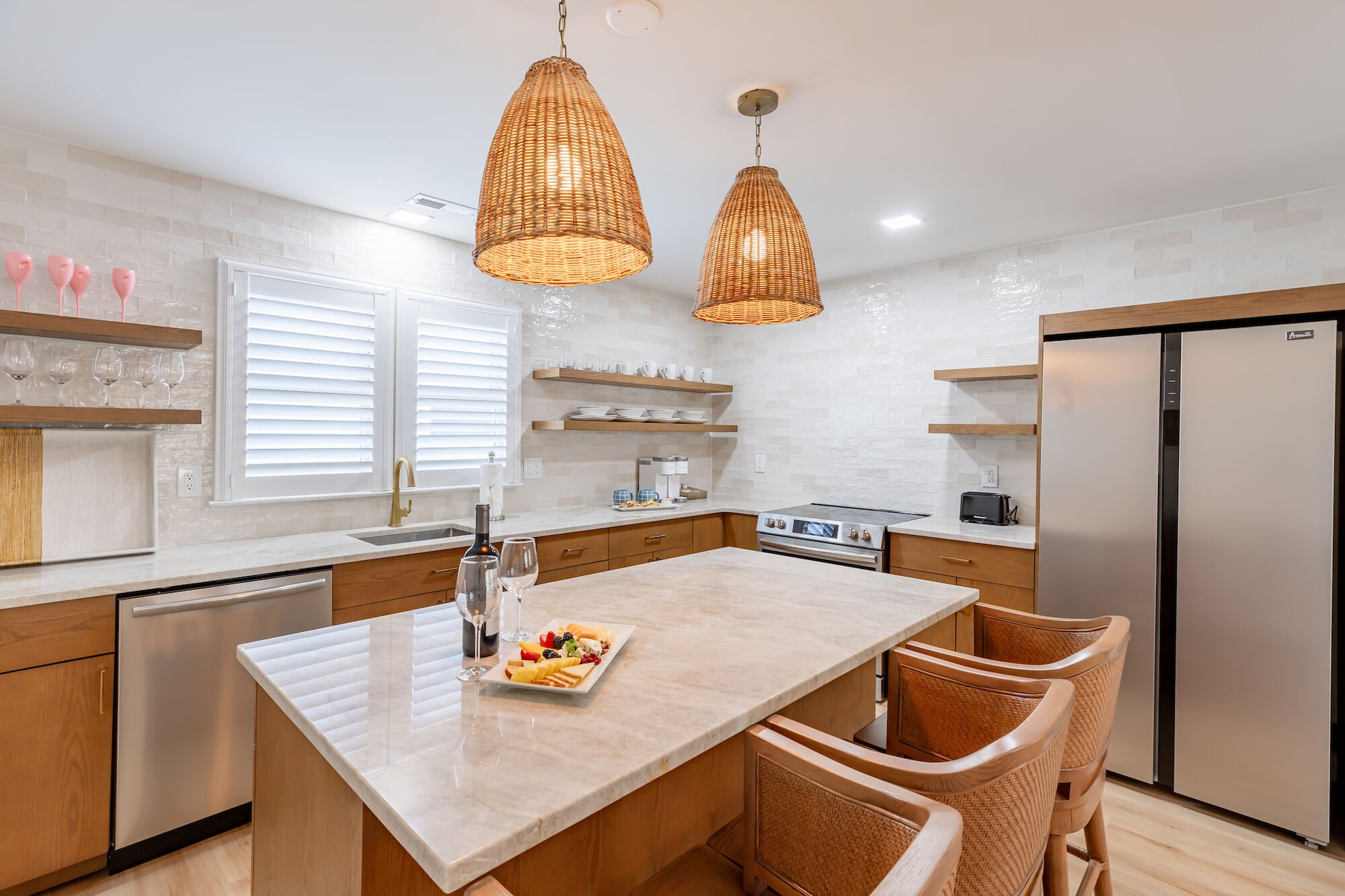 A modern kitchen with wooden cabinets, an island with barstools, hanging wicker lights, stainless steel appliances, and a tray of food on the counter.