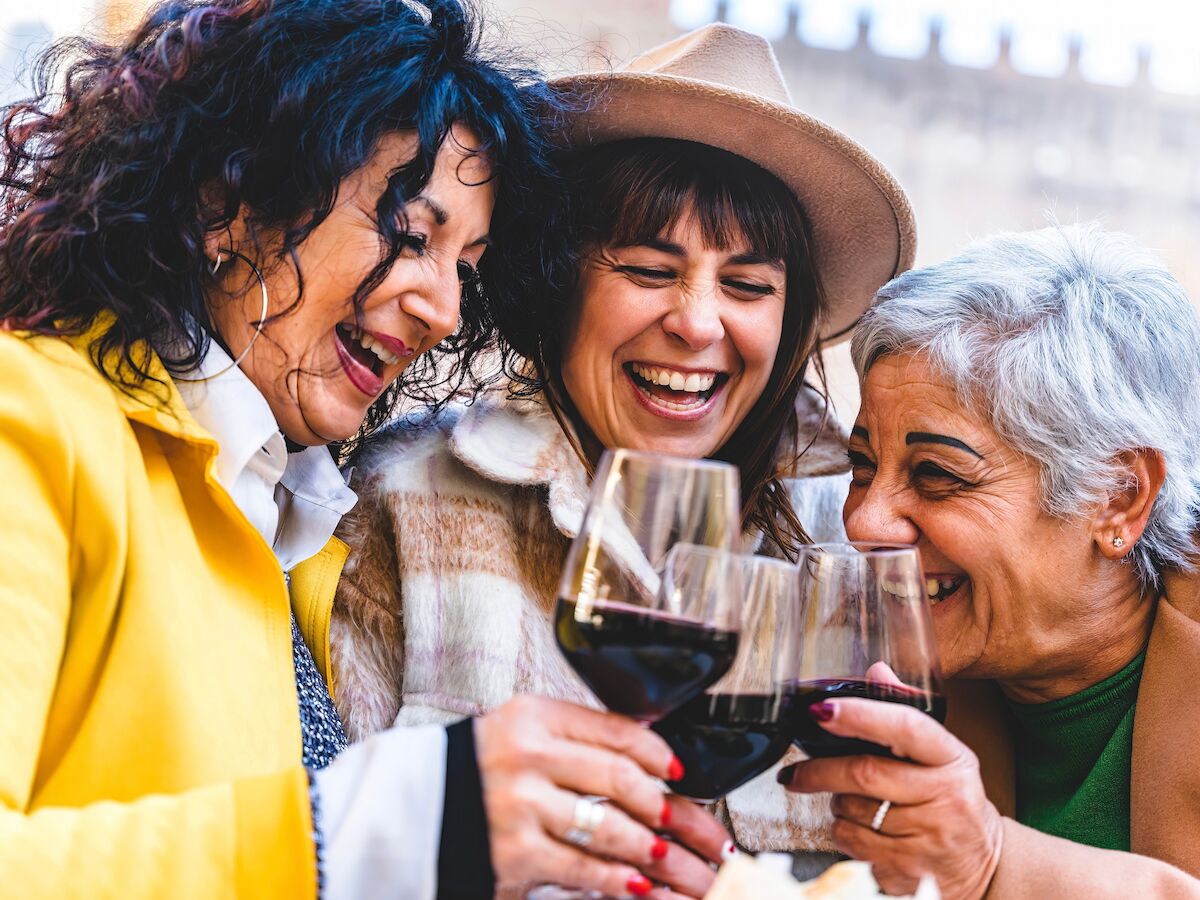Three people are smiling and toasting with wine glasses.