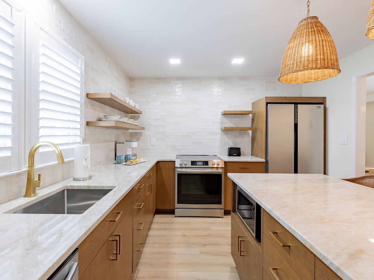 A modern kitchen featuring wooden cabinets, marble countertops, stainless steel appliances, and two wicker pendant lights over an island.