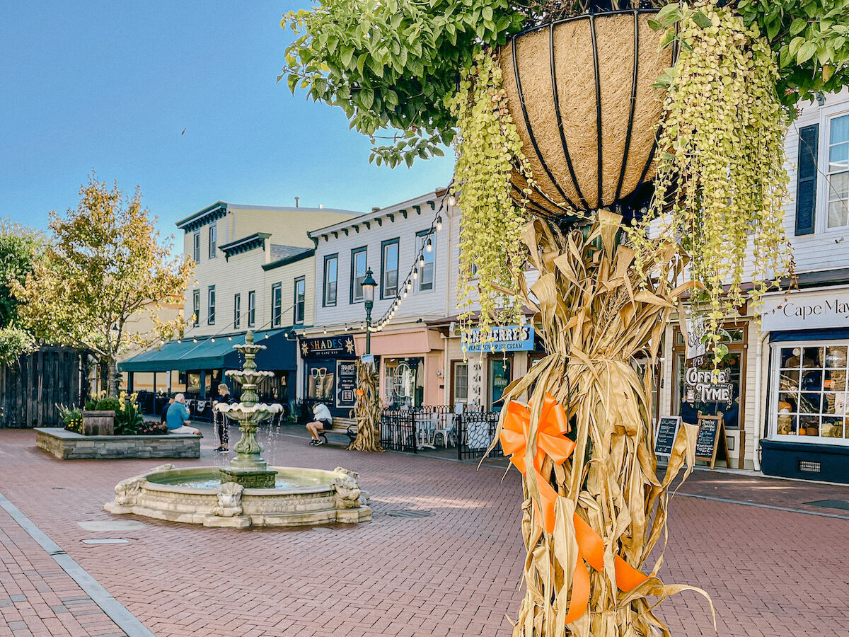 A charming street scene featuring a fountain, quaint shops, and a decorated post with greenery and ribbons.