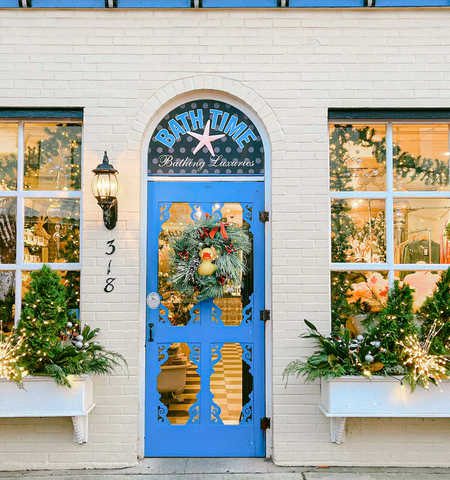 A festive storefront decorated with greenery, lights, and a wreath on a blue door, with 