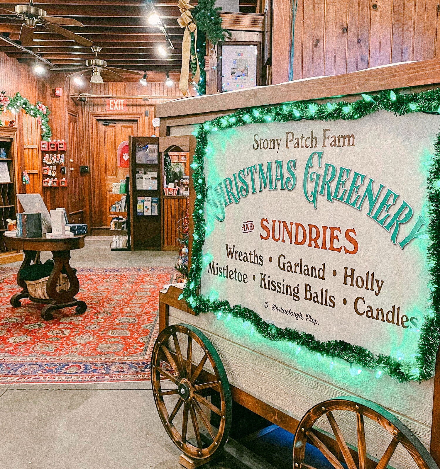 A cozy store interior with a cart selling Christmas greenery and sundries, decorated with festive wreaths and garlands.