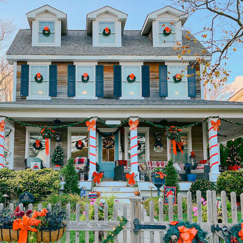 A house decorated for Christmas with ribbons, wreaths, and lights on the porch and fence.