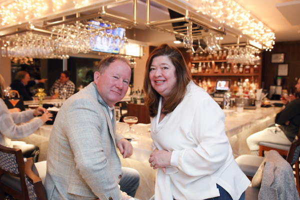 A couple is sitting in a brightly lit bar with people socializing in the background.