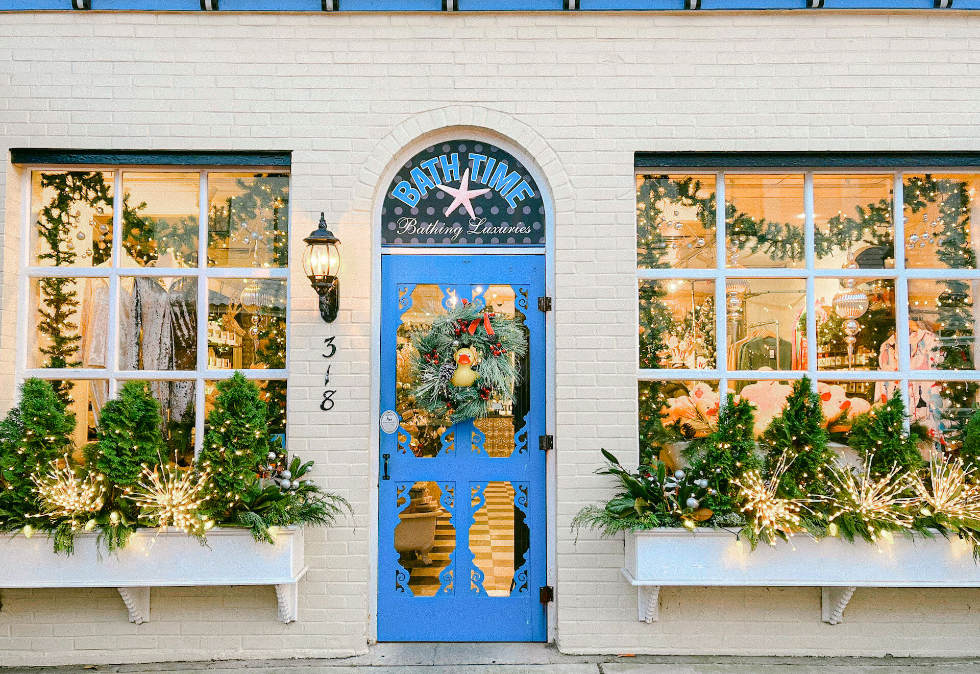 A festive storefront with a blue door, holiday wreath, and decorated windows with greenery and lights, labeled "Bath Time."