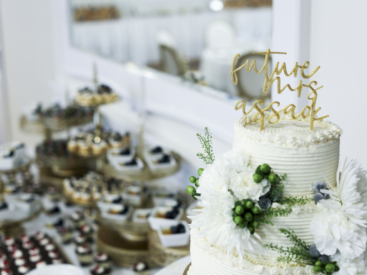 A decorated wedding cake with "Future Mrs Assad" topper and various desserts are displayed in the background.