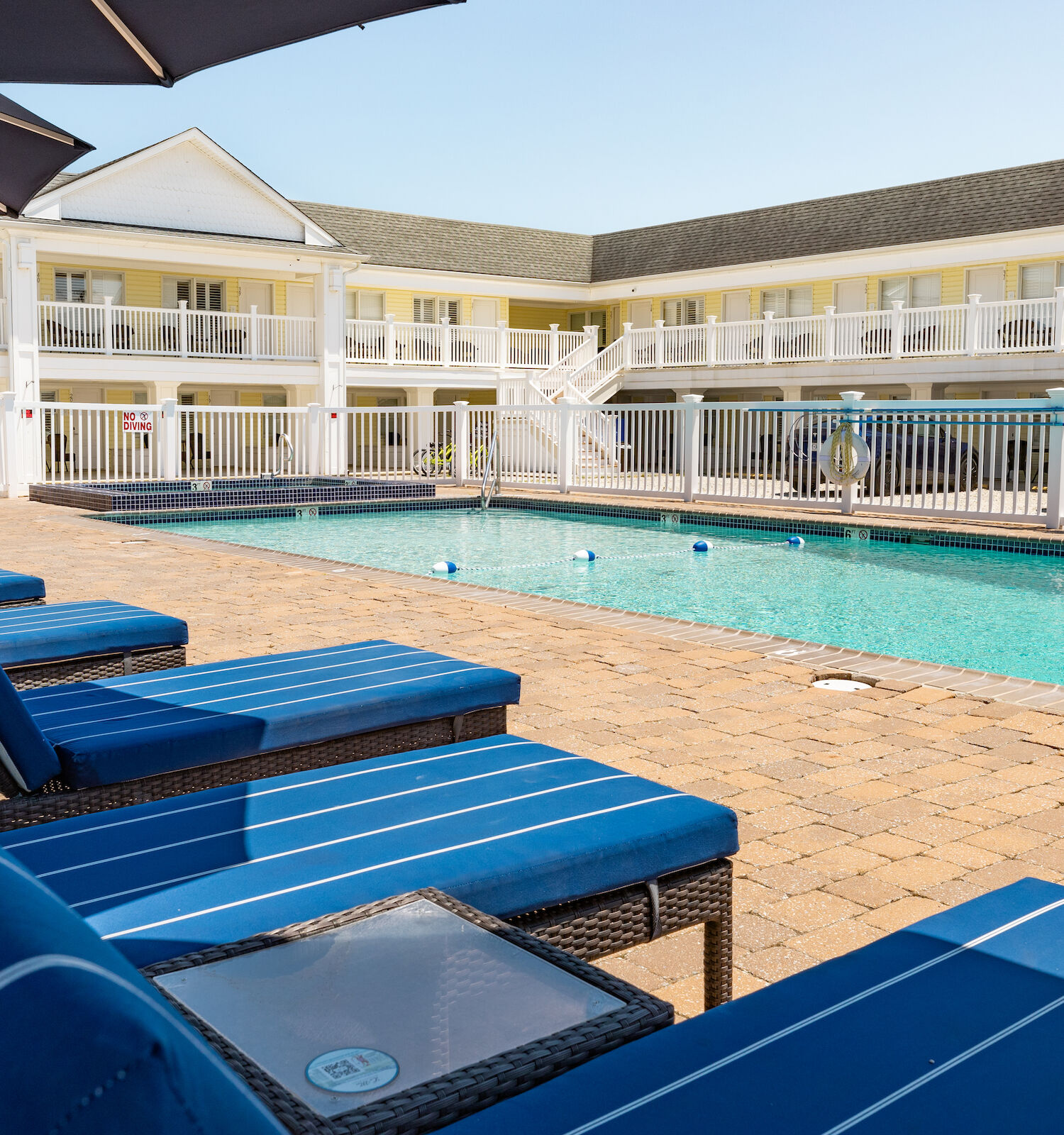 A hotel courtyard with a pool, blue cushioned lounge chairs, and an upper-level balcony around the perimeter.