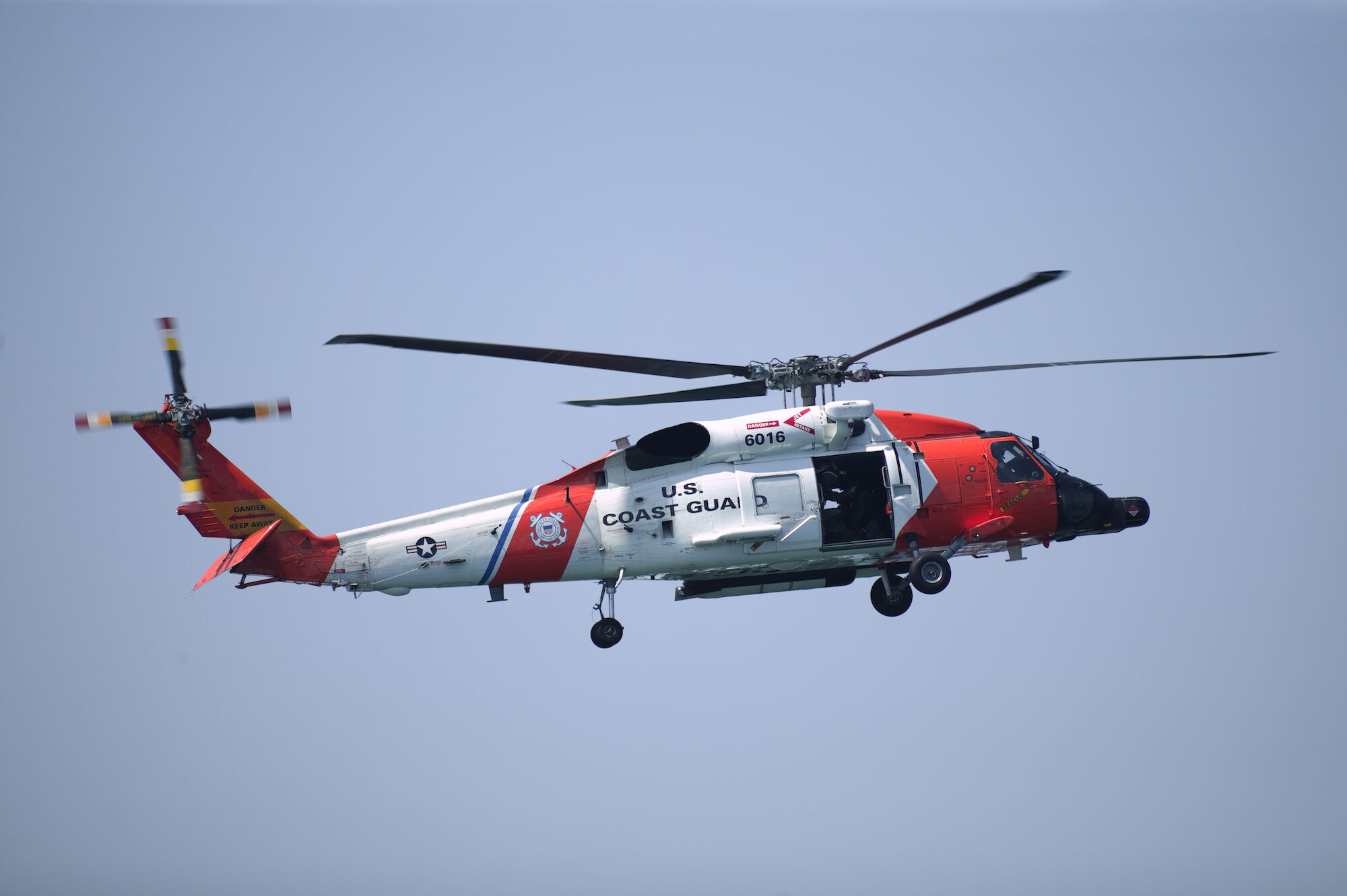 A U.S. Coast Guard helicopter is flying against a clear blue sky.