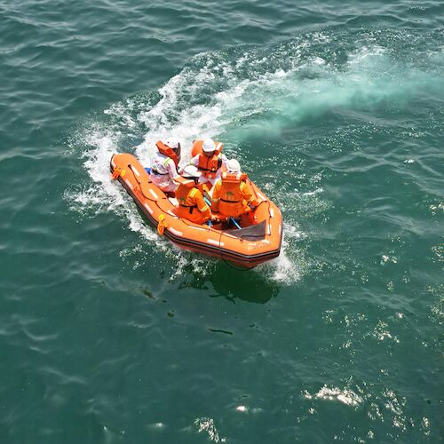 A group of people wearing orange life jackets are riding in a small inflatable boat on the water.