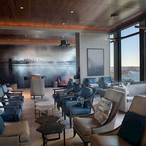A modern lounge with comfortable seating, large windows offering a scenic view of a waterfront and a Ferris wheel in the distance, ending the sentence.