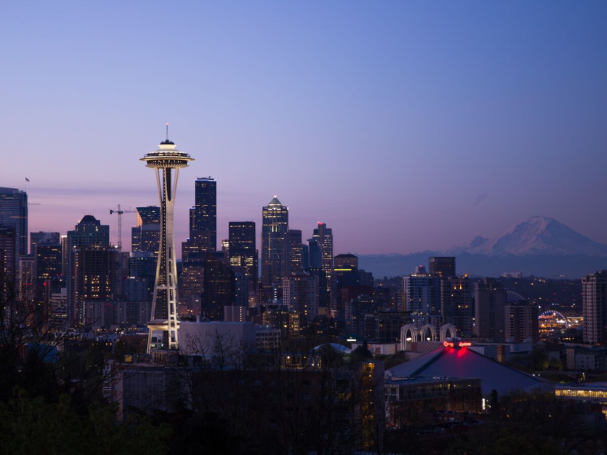 This image shows the Seattle skyline at dusk, featuring the Space Needle prominently and Mount Rainier in the background.