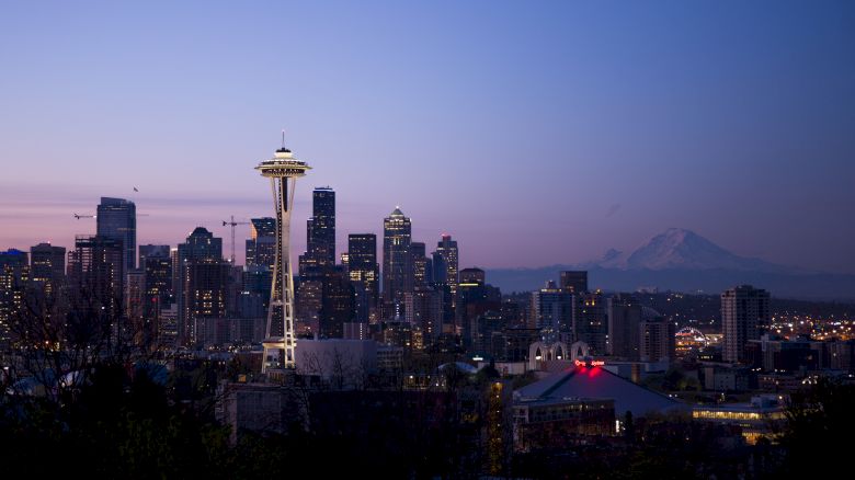 This image shows the Seattle skyline at dusk, featuring the Space Needle prominently and Mount Rainier in the background.