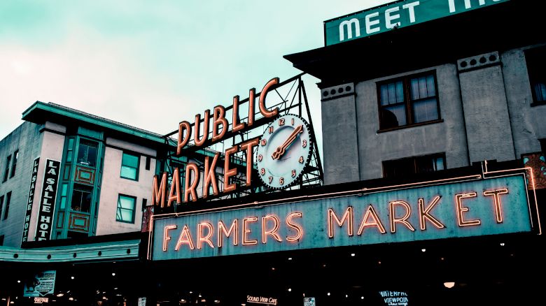 The image shows the iconic "Public Market Center" sign with a clock and a neon "Farmers Market" sign, indicating a popular market area.
